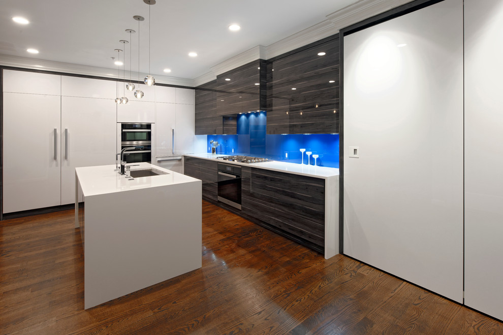 Inredning av ett modernt stort kök, med en enkel diskho, släta luckor, bänkskiva i kvarts, blått stänkskydd, glaspanel som stänkskydd, rostfria vitvaror, mellanmörkt trägolv, en köksö och vita skåp