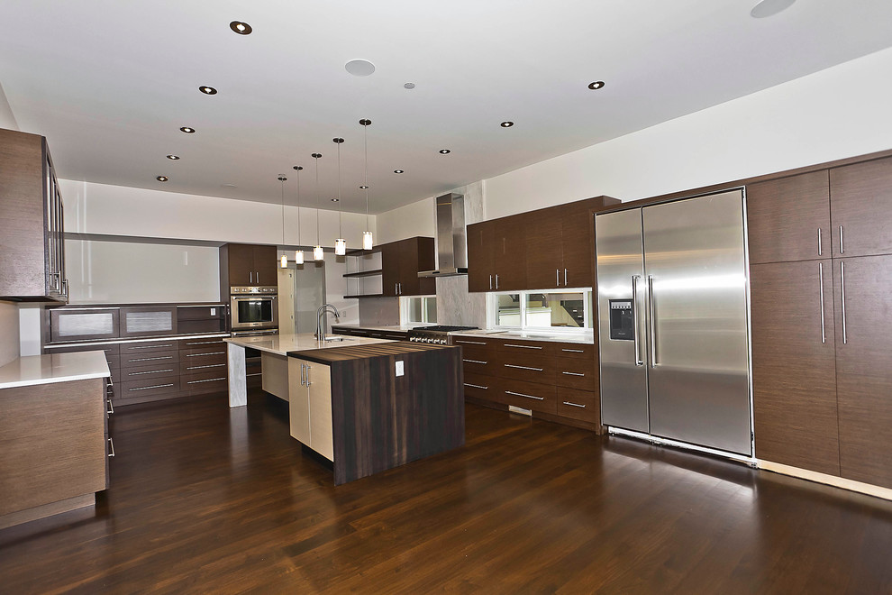 This is an example of a large contemporary l-shaped kitchen/diner in DC Metro with a submerged sink, flat-panel cabinets, dark wood cabinets, stone slab splashback, stainless steel appliances, dark hardwood flooring, an island, marble worktops, white splashback and brown floors.