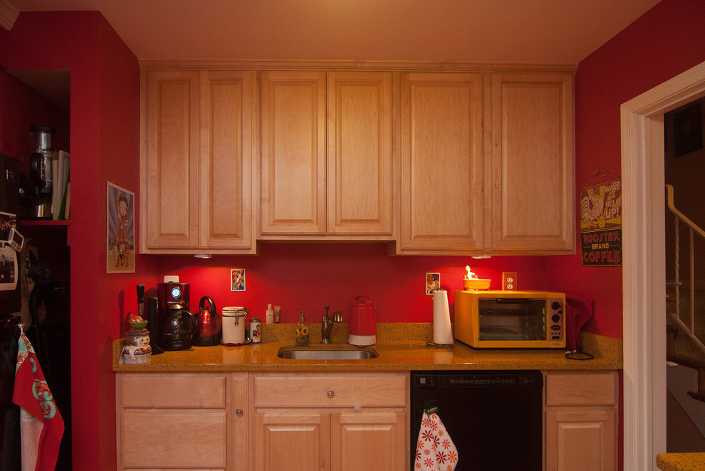 Modelo de cocina comedor ecléctica de tamaño medio con armarios con paneles con relieve, puertas de armario beige, encimera de granito, electrodomésticos negros, suelo vinílico, península, fregadero encastrado y salpicadero rojo