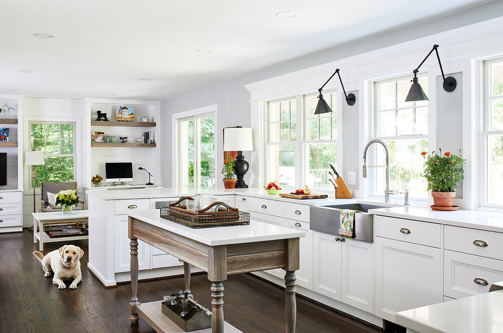 Modelo de cocina de tamaño medio con salpicadero blanco, electrodomésticos de acero inoxidable, suelo de madera oscura, una isla y encimeras blancas