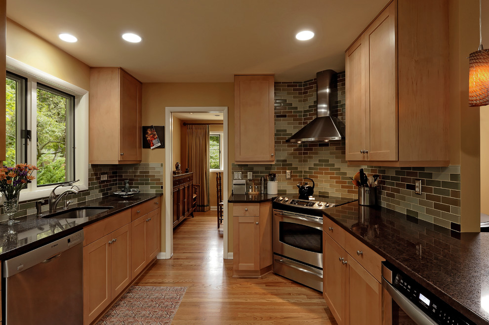 Modelo de cocinas en U clásico con electrodomésticos de acero inoxidable, fregadero bajoencimera, armarios estilo shaker, puertas de armario de madera oscura, salpicadero multicolor y salpicadero de azulejos tipo metro