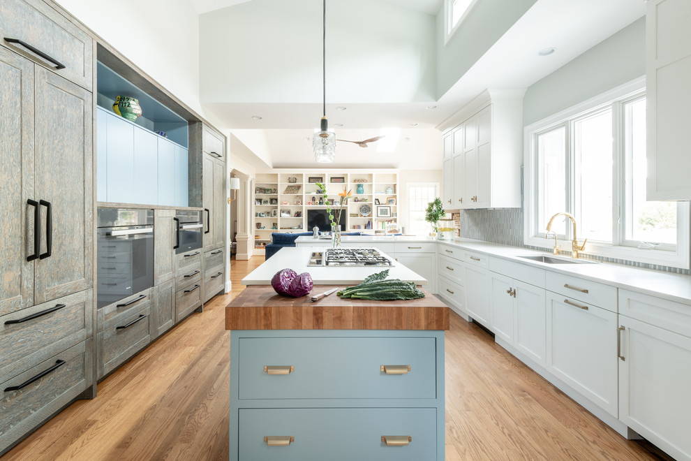 ワシントンD.C.にある高級な広いトランジショナルスタイルのおしゃれなキッチン (シェーカースタイル扉のキャビネット、青いキッチンパネル、セラミックタイルのキッチンパネル、パネルと同色の調理設備、アンダーカウンターシンク、白いキャビネット、無垢フローリング、茶色い床、白いキッチンカウンター) の写真