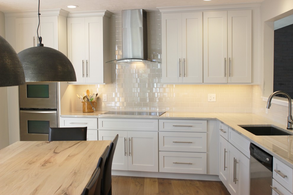 Inspiration for a large transitional u-shaped light wood floor eat-in kitchen remodel in Chicago with an undermount sink, flat-panel cabinets, white cabinets, granite countertops, beige backsplash, subway tile backsplash and stainless steel appliances