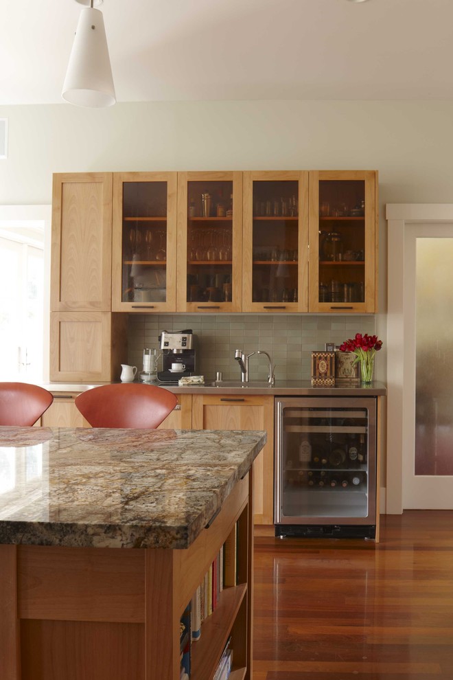 Klassisk inredning av ett kök, med granitbänkskiva, rostfria vitvaror, luckor med glaspanel, skåp i mellenmörkt trä och grått stänkskydd