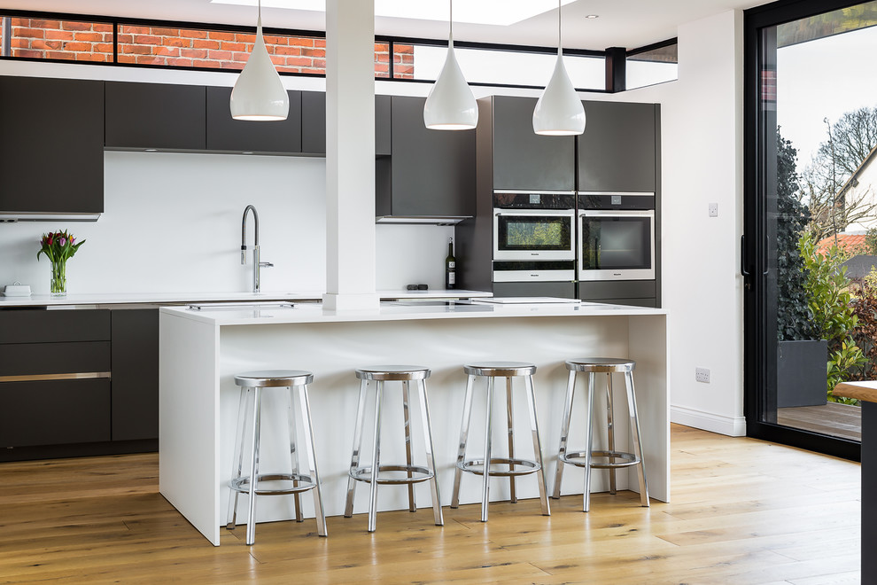 Zweizeilige Moderne Küche mit flächenbündigen Schrankfronten, schwarzen Schränken, hellem Holzboden, Kücheninsel, beigem Boden und weißer Arbeitsplatte in Sonstige