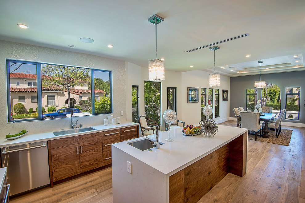 This is an example of a large modern u-shaped kitchen/diner in Los Angeles with a submerged sink, flat-panel cabinets, white cabinets, composite countertops, white splashback, stainless steel appliances, medium hardwood flooring, an island and brown floors.