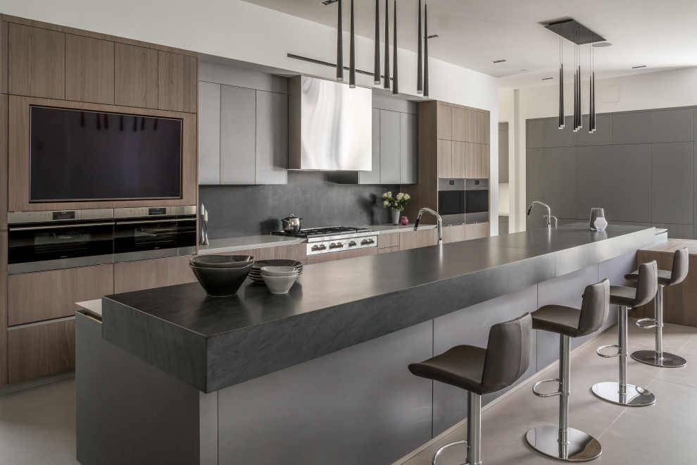 Moderne Küche mit flächenbündigen Schrankfronten, dunklen Holzschränken, Küchenrückwand in Schwarz, Küchengeräten aus Edelstahl, Kücheninsel, grauem Boden und grauer Arbeitsplatte in Los Angeles
