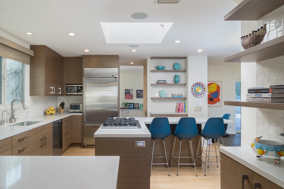 Example of a mid-sized mid-century modern u-shaped light wood floor and beige floor open concept kitchen design in Los Angeles with an undermount sink, flat-panel cabinets, medium tone wood cabinets, quartz countertops, white backsplash, ceramic backsplash, stainless steel appliances and an island