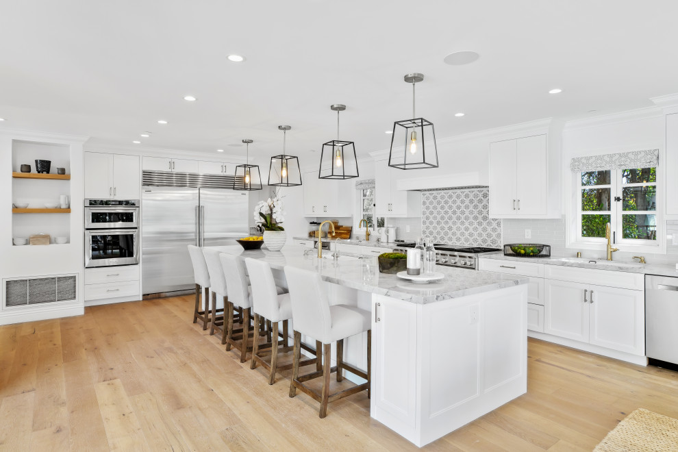 Traditional l-shaped kitchen in Los Angeles with a submerged sink, recessed-panel cabinets, white cabinets, grey splashback, stainless steel appliances, light hardwood flooring, an island, beige floors and grey worktops.