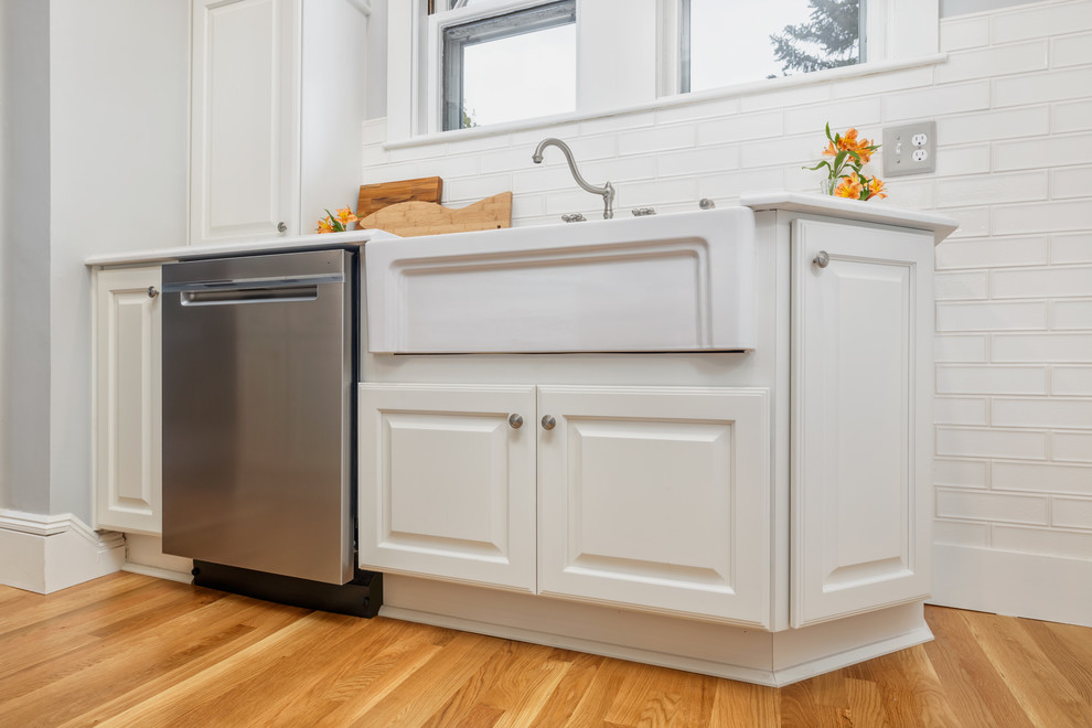 Exempel på ett mellanstort klassiskt vit vitt kök, med en rustik diskho, luckor med upphöjd panel, vita skåp, bänkskiva i kvartsit, vitt stänkskydd, stänkskydd i tunnelbanekakel, rostfria vitvaror, mellanmörkt trägolv, en köksö och beiget golv