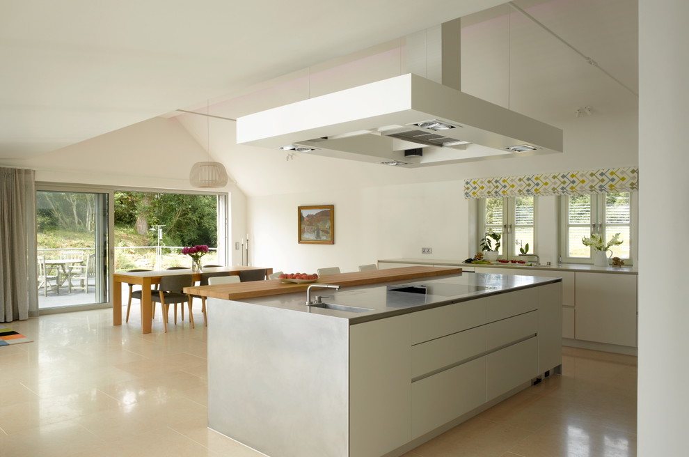 Modern inredning av ett stort kök med öppen planlösning, med släta luckor, vita skåp, bänkskiva i rostfritt stål, en köksö och beiget golv
