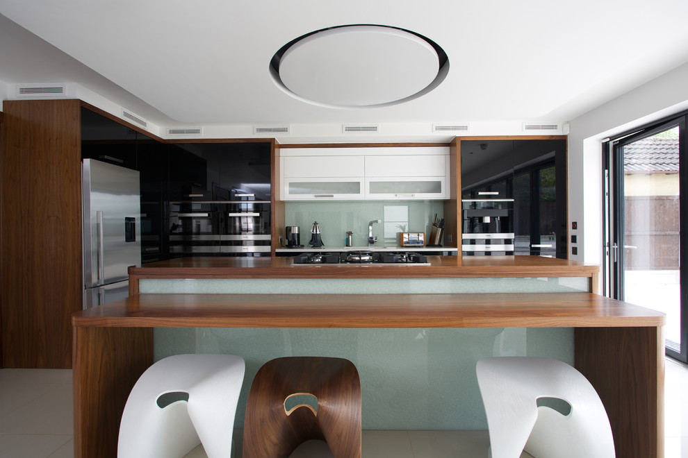 Foto på ett funkis kök, med släta luckor, grått stänkskydd, glaspanel som stänkskydd, rostfria vitvaror, flera köksöar och träbänkskiva