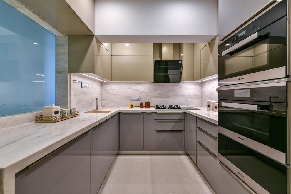 Inspiration for a world-inspired u-shaped kitchen in Mumbai with a submerged sink, flat-panel cabinets, grey cabinets, beige splashback, stainless steel appliances, beige floors and beige worktops.
