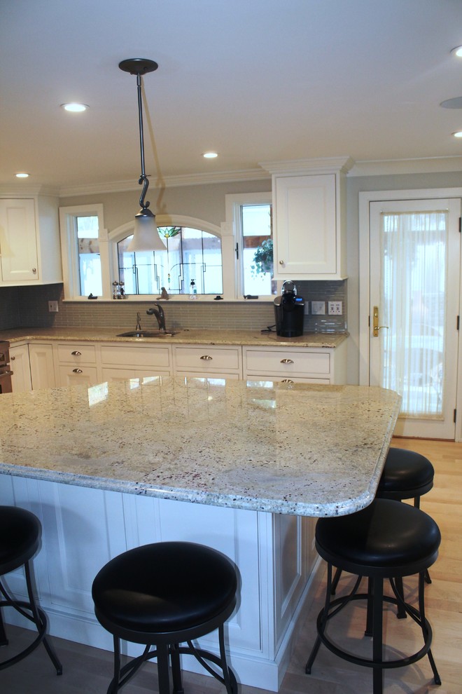 Exempel på ett klassiskt kök, med en undermonterad diskho, vita skåp, granitbänkskiva, grått stänkskydd, stänkskydd i glaskakel och rostfria vitvaror