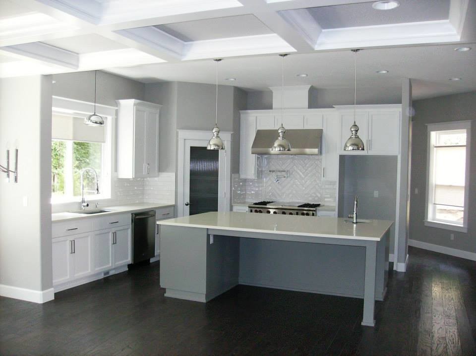 Foto på ett funkis l-kök, med en undermonterad diskho, skåp i shakerstil, vita skåp, bänkskiva i kvarts, vitt stänkskydd, stänkskydd i keramik, rostfria vitvaror, mörkt trägolv och en köksö