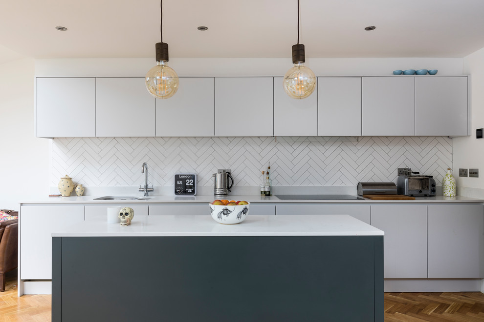 Mittelgroße Moderne Küche mit Doppelwaschbecken, flächenbündigen Schrankfronten, weißen Schränken, Küchenrückwand in Weiß, Rückwand aus Keramikfliesen, braunem Holzboden und Kücheninsel in London