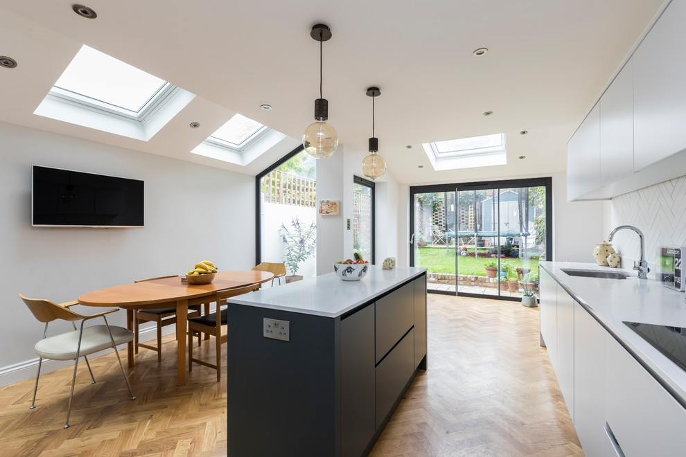 This is an example of a medium sized contemporary single-wall kitchen in London with a double-bowl sink, flat-panel cabinets, white cabinets, white splashback, ceramic splashback, medium hardwood flooring, an island and brown floors.