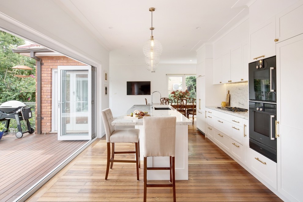 Ejemplo de cocina lineal, clásica renovada, de tamaño medio, con armarios estilo shaker, puertas de armario blancas, encimera de granito, salpicadero verde, electrodomésticos negros, suelo de madera en tonos medios, una isla, fregadero de un seno y encimeras grises
