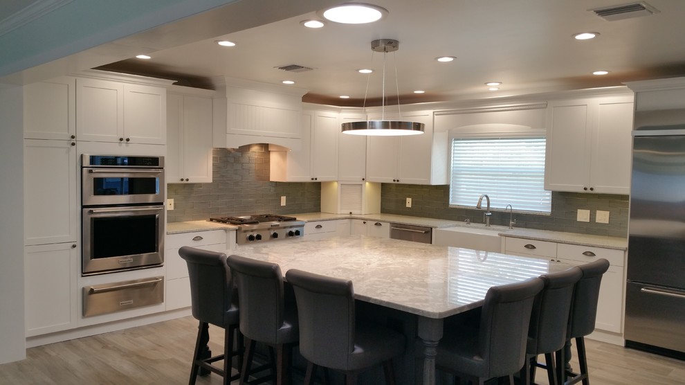 Inspiration for a large rural l-shaped enclosed kitchen in Tampa with a belfast sink, shaker cabinets, white cabinets, engineered stone countertops, grey splashback, glass tiled splashback, stainless steel appliances, porcelain flooring and an island.