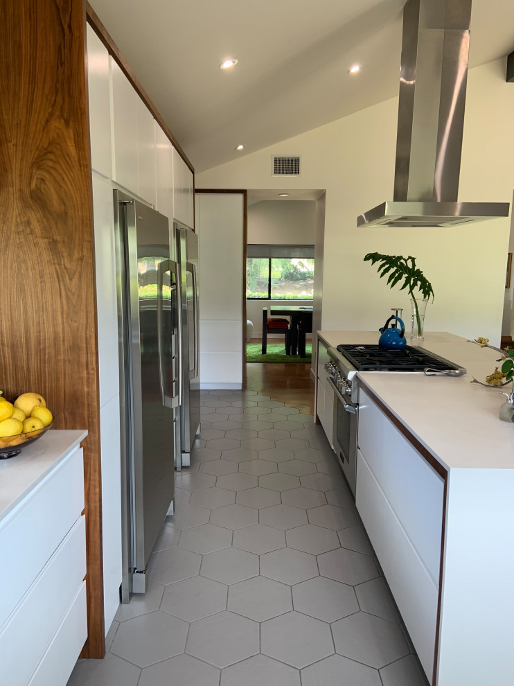 Example of a mid-sized 1960s l-shaped porcelain tile, gray floor and vaulted ceiling open concept kitchen design in San Diego with an undermount sink, flat-panel cabinets, white cabinets, quartz countertops, white backsplash, quartz backsplash, stainless steel appliances, an island and white countertops