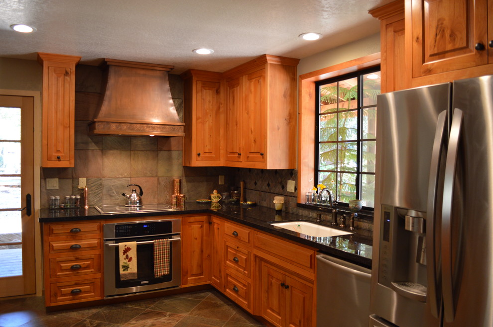 Foto på ett mellanstort amerikanskt kök, med en enkel diskho, luckor med upphöjd panel, skåp i mellenmörkt trä, bänkskiva i kvartsit, grått stänkskydd, stänkskydd i stenkakel, rostfria vitvaror, skiffergolv, brunt golv och en halv köksö