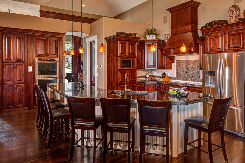 Mid-sized elegant l-shaped dark wood floor and brown floor open concept kitchen photo in Salt Lake City with brown cabinets, granite countertops, brown backsplash, mosaic tile backsplash, stainless steel appliances, an island, an undermount sink and raised-panel cabinets