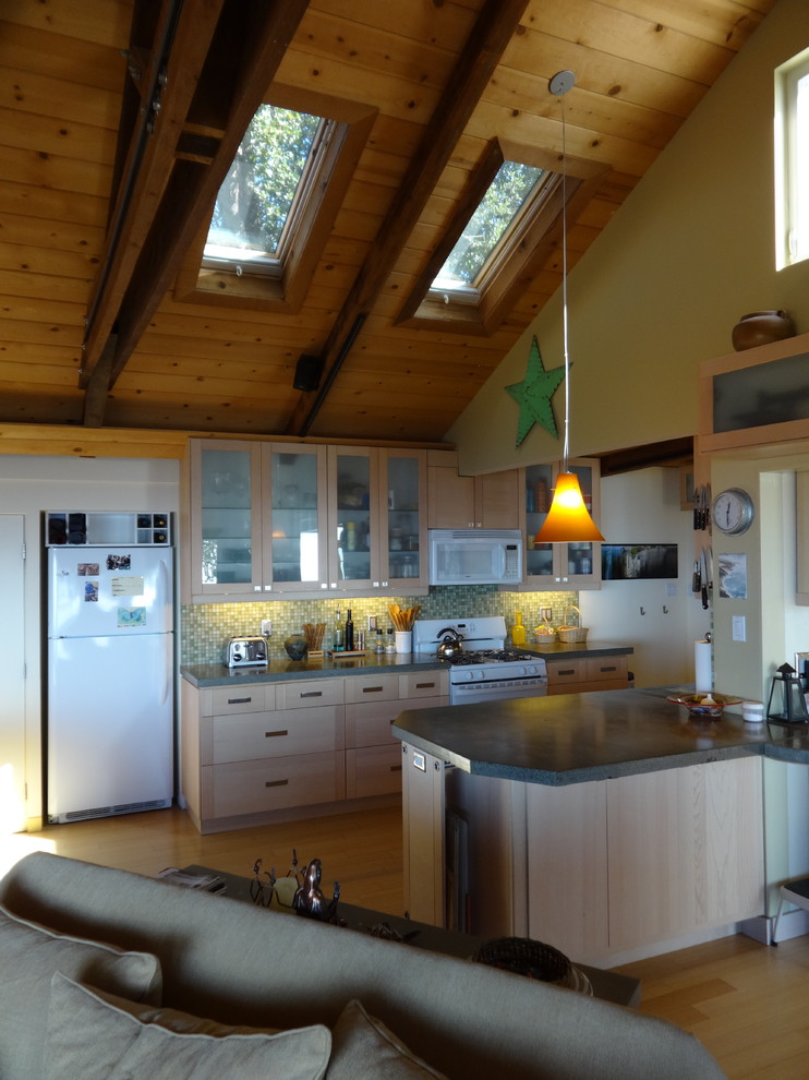 Exemple d'une cuisine ouverte bord de mer avec un placard à porte vitrée, des portes de placard grises, un plan de travail en béton, une crédence grise, un électroménager blanc et un sol en bois brun.
