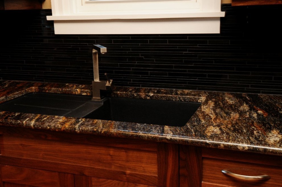 Cette image montre une cuisine américaine design en U et bois brun avec un évier encastré, un placard à porte shaker, un plan de travail en granite, une crédence noire, une crédence en carrelage de pierre et un électroménager en acier inoxydable.