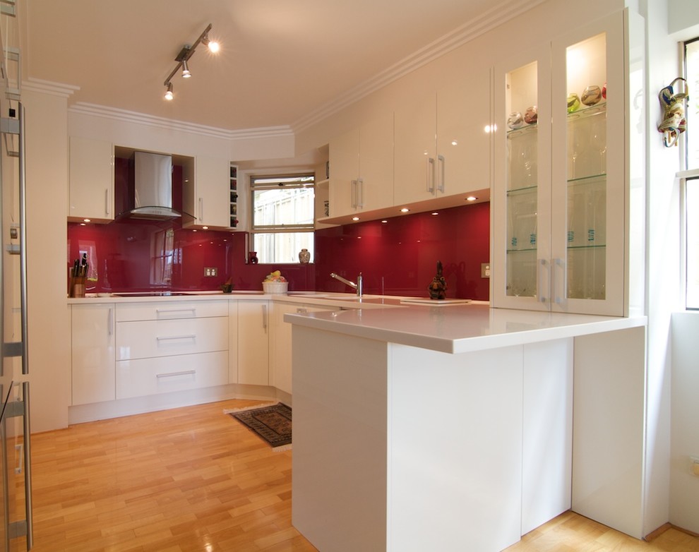 Inspiration for a small modern u-shaped light wood floor enclosed kitchen remodel in Sydney with an integrated sink, flat-panel cabinets, white cabinets, solid surface countertops, red backsplash, glass sheet backsplash, stainless steel appliances and no island