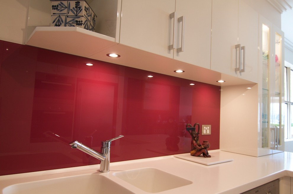 Modern inredning av ett avskilt, litet u-kök, med en integrerad diskho, släta luckor, vita skåp, bänkskiva i koppar, rött stänkskydd, glaspanel som stänkskydd, rostfria vitvaror och ljust trägolv