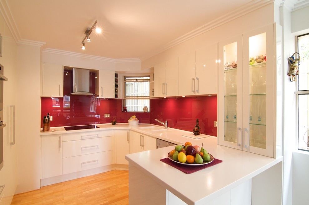 Small minimalist u-shaped light wood floor enclosed kitchen photo in Sydney with an integrated sink, flat-panel cabinets, white cabinets, solid surface countertops, red backsplash, glass sheet backsplash, stainless steel appliances and no island
