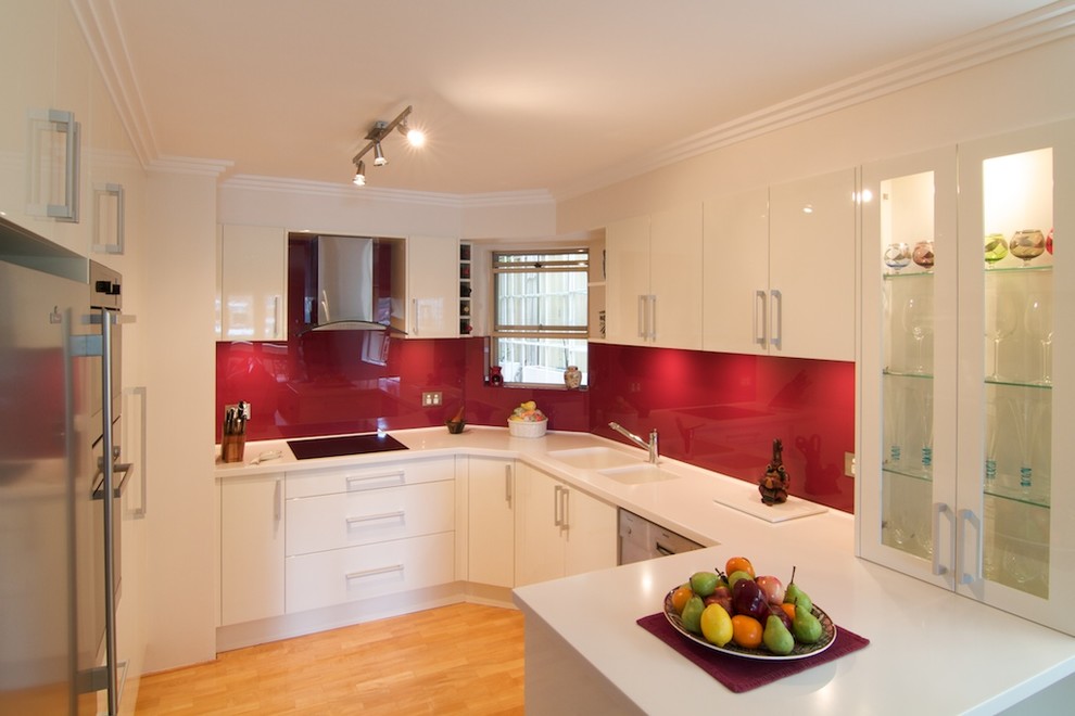 Exempel på ett avskilt, litet modernt u-kök, med en integrerad diskho, släta luckor, vita skåp, bänkskiva i koppar, rött stänkskydd, glaspanel som stänkskydd, rostfria vitvaror och ljust trägolv
