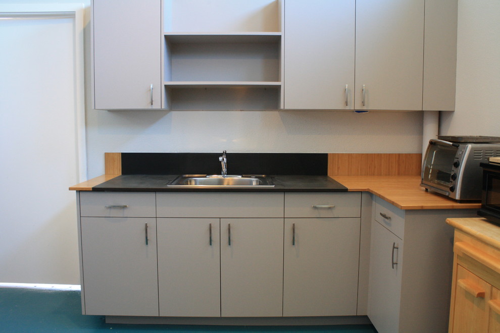 Bild på ett mellanstort, avskilt funkis flerfärgad flerfärgat l-kök, med heltäckningsmatta, grått golv, släta luckor, grå skåp, träbänkskiva, en nedsänkt diskho och flerfärgad stänkskydd