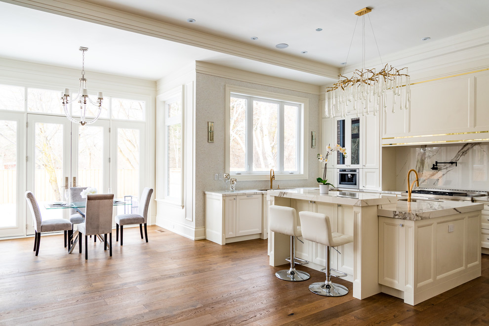 Foto på ett stort vintage vit kök, med en dubbel diskho, luckor med infälld panel, vita skåp, marmorbänkskiva, vitt stänkskydd, stänkskydd i marmor, rostfria vitvaror, mellanmörkt trägolv, en köksö och brunt golv