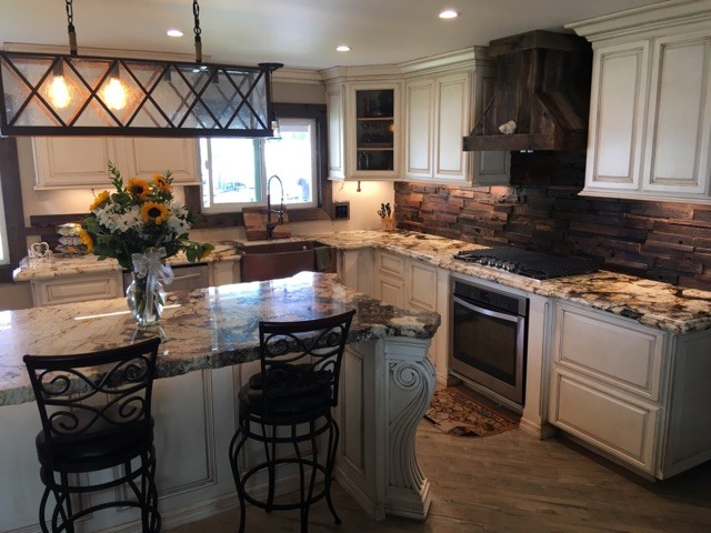 Large rural l-shaped kitchen/diner in Los Angeles with a belfast sink, shaker cabinets, white cabinets, onyx worktops, brown splashback, stone tiled splashback, stainless steel appliances, medium hardwood flooring and an island.