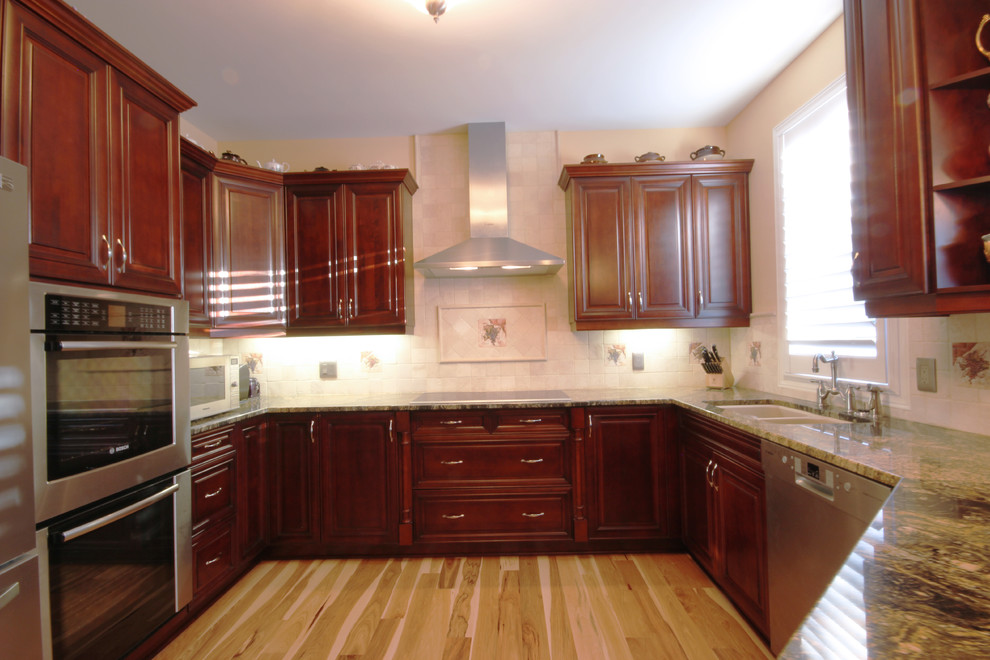 Exempel på ett stort kök, med en dubbel diskho, luckor med profilerade fronter, skåp i mörkt trä, granitbänkskiva, gult stänkskydd, stänkskydd i stenkakel, rostfria vitvaror, mellanmörkt trägolv och en halv köksö