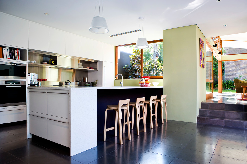 Modern inredning av ett litet kök, med en undermonterad diskho, släta luckor, vita skåp, granitbänkskiva, stänkskydd med metallisk yta, stänkskydd i metallkakel, rostfria vitvaror, skiffergolv, en halv köksö och svart golv