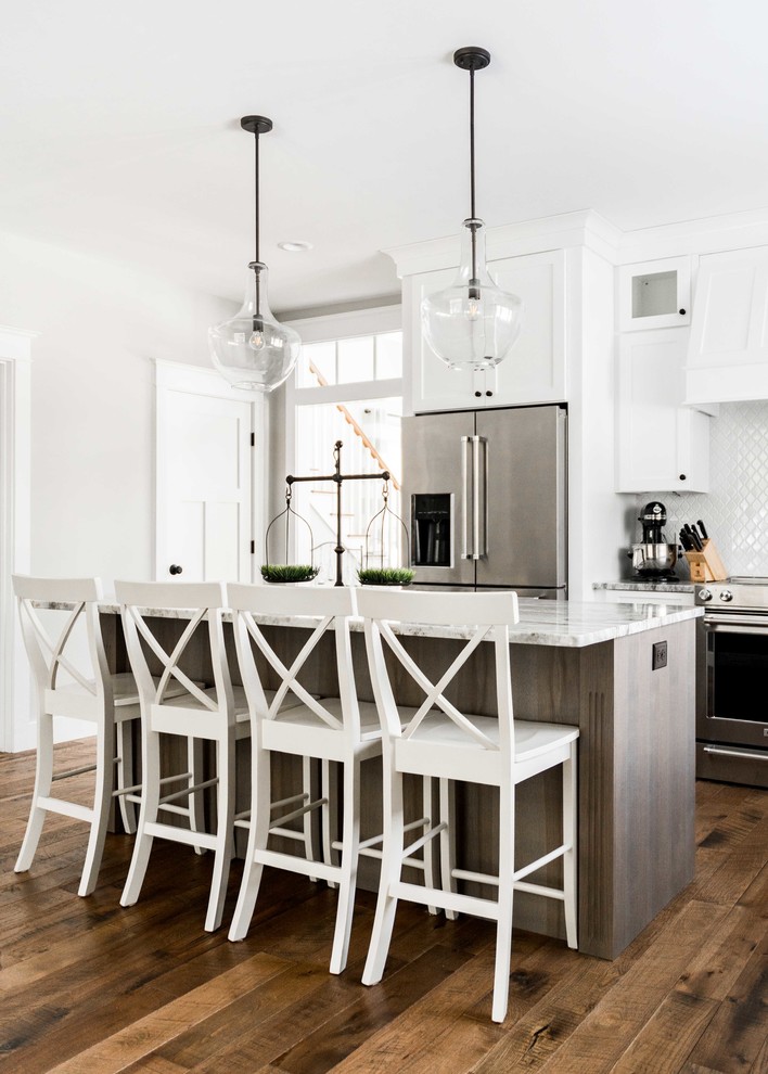 Large cottage l-shaped medium tone wood floor and brown floor eat-in kitchen photo in Portland Maine with a farmhouse sink, shaker cabinets, gray cabinets, granite countertops, white backsplash, mosaic tile backsplash, stainless steel appliances, an island and gray countertops