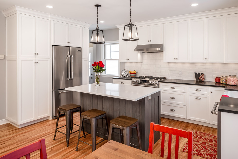 Inspiration for a mid-sized contemporary l-shaped medium tone wood floor eat-in kitchen remodel in Minneapolis with a farmhouse sink, shaker cabinets, white cabinets, white backsplash, stainless steel appliances, an island, solid surface countertops and subway tile backsplash