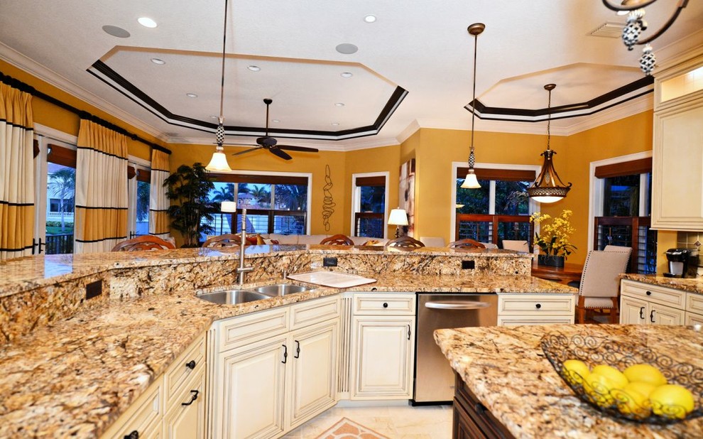 Inspiration for a large mediterranean l-shaped open plan kitchen in Tampa with a built-in sink, raised-panel cabinets, dark wood cabinets, granite worktops, stainless steel appliances, limestone flooring and multiple islands.