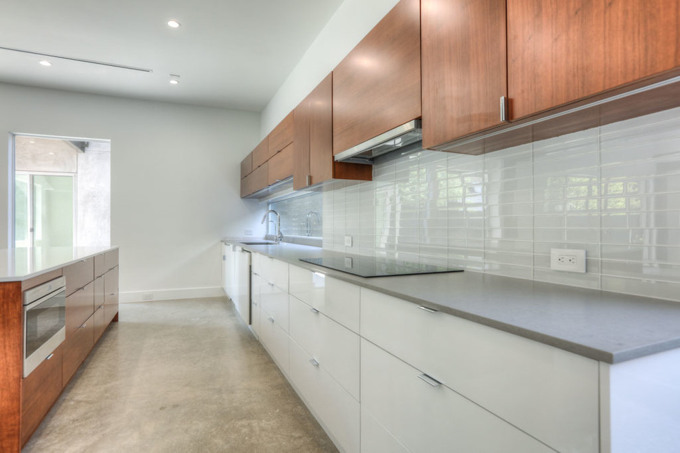 Mid-sized minimalist l-shaped concrete floor and gray floor enclosed kitchen photo in Houston with a farmhouse sink, flat-panel cabinets, solid surface countertops, white backsplash, porcelain backsplash, an island, white cabinets and stainless steel appliances