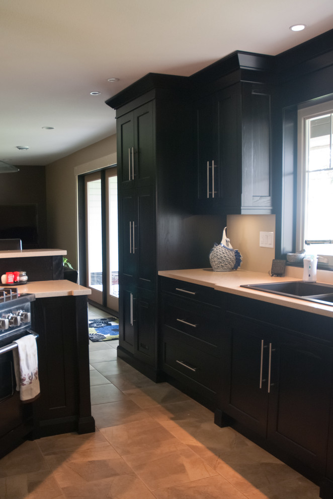 Modelo de cocina contemporánea con fregadero encastrado, armarios estilo shaker, puertas de armario negras, encimera de cuarzo compacto, electrodomésticos negros y suelo de baldosas de cerámica