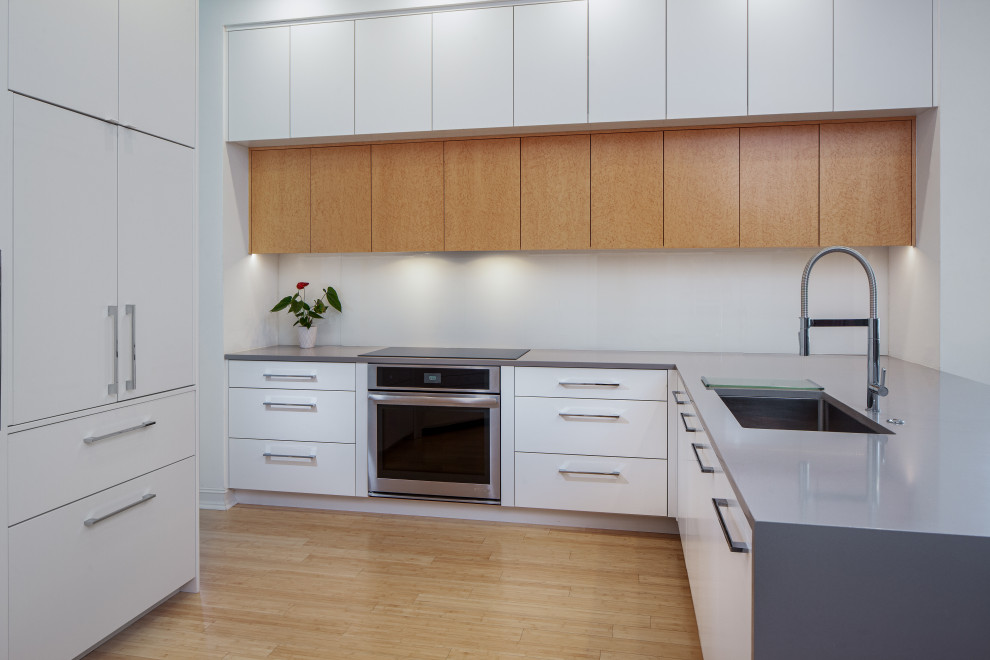 マイアミにある高級な小さなコンテンポラリースタイルのおしゃれなキッチン (アンダーカウンターシンク、フラットパネル扉のキャビネット、白いキャビネット、クオーツストーンカウンター、白いキッチンパネル、ガラス板のキッチンパネル、パネルと同色の調理設備、竹フローリング、黄色い床、グレーのキッチンカウンター) の写真