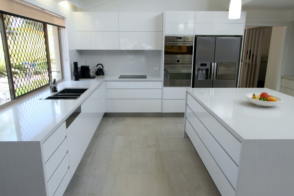 Exempel på ett mellanstort modernt kök, med en dubbel diskho, släta luckor, vita skåp, bänkskiva i kvarts, vitt stänkskydd, stänkskydd i porslinskakel, rostfria vitvaror, klinkergolv i keramik och en köksö