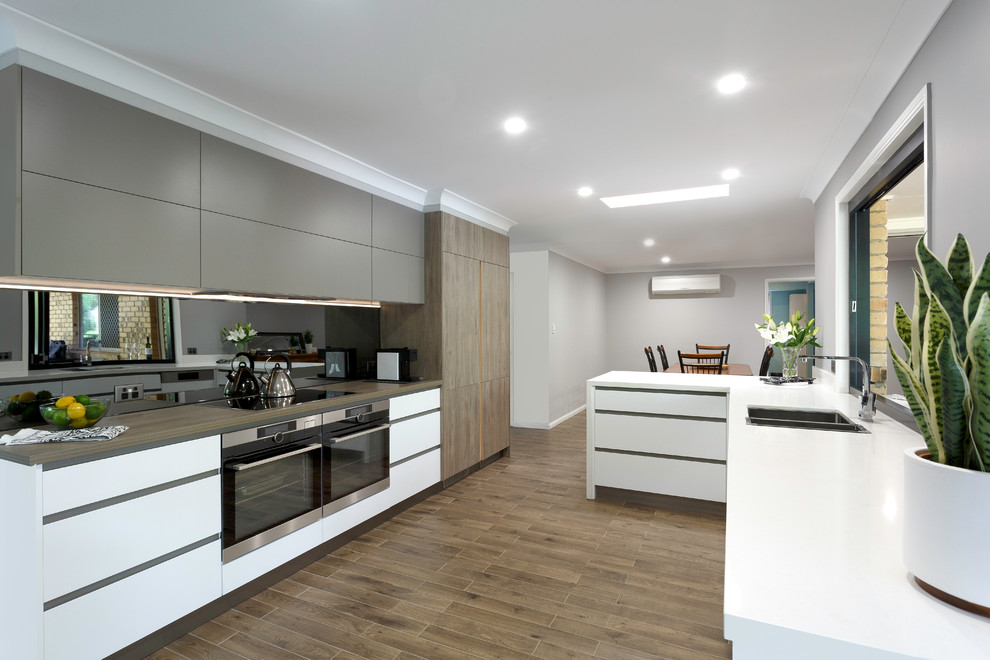 Idéer för ett stort modernt vit kök, med släta luckor, mellanmörkt trägolv, brunt golv, en dubbel diskho, grå skåp, svart stänkskydd, glaspanel som stänkskydd, svarta vitvaror och en halv köksö