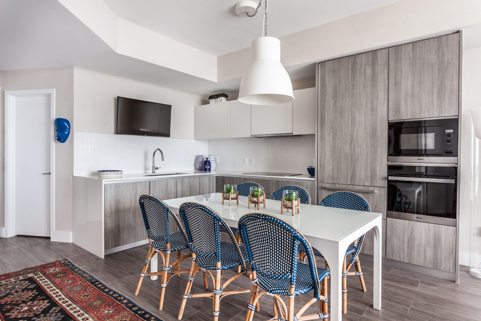 Small beach style l-shaped kitchen/diner in Miami with white splashback, stainless steel appliances, a submerged sink, flat-panel cabinets, grey cabinets and grey floors.
