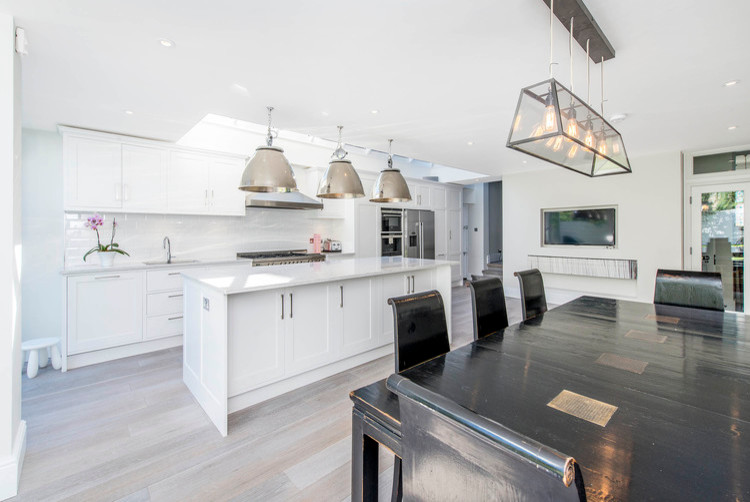 Example of a mid-sized trendy single-wall light wood floor eat-in kitchen design in London with an undermount sink, recessed-panel cabinets, white cabinets, granite countertops, white backsplash, subway tile backsplash, stainless steel appliances and an island