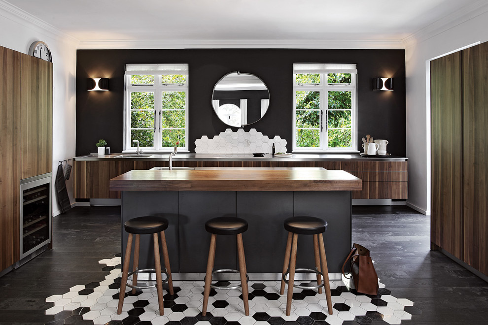 Moderne Küche mit flächenbündigen Schrankfronten, dunklen Holzschränken, Edelstahl-Arbeitsplatte, Küchenrückwand in Weiß, dunklem Holzboden, Kücheninsel, schwarzem Boden und grauer Arbeitsplatte in Sonstige