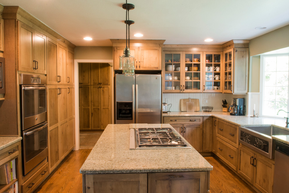 Example of a mid-sized mountain style u-shaped medium tone wood floor and brown floor enclosed kitchen design in Other with a farmhouse sink, shaker cabinets, medium tone wood cabinets, granite countertops, beige backsplash, ceramic backsplash, stainless steel appliances and an island