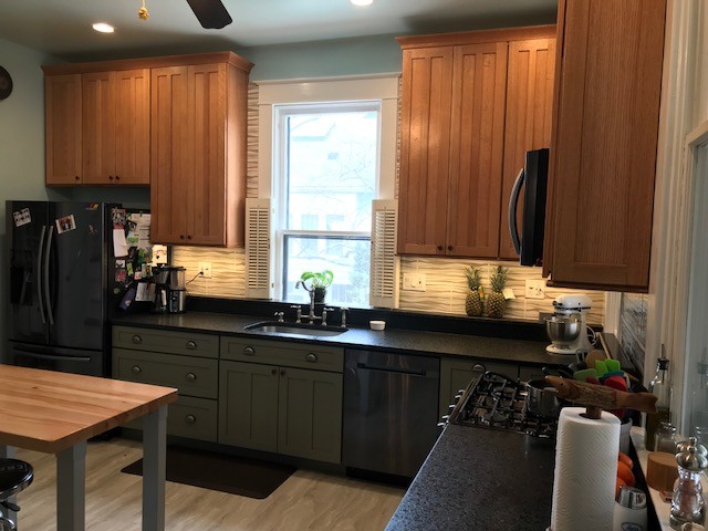 Amerikansk inredning av ett mellanstort kök, med en undermonterad diskho, skåp i shakerstil, gröna skåp, granitbänkskiva, beige stänkskydd, stänkskydd i keramik, rostfria vitvaror, målat trägolv, en köksö och grått golv